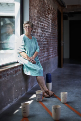 ceramic artist sitting on windowsill with her artwork in front of her