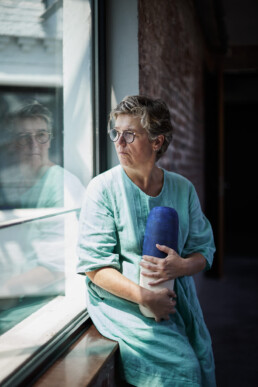 ceramic artist sitting on windowsill gazing out the window and holding her work