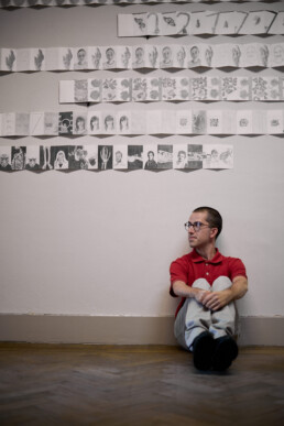 artist sitting against the wall with his pencil drawings hanging on the wall